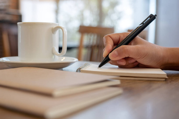 Kafe 'de kahve fincanı ile boş bir deftere el yazısının yakın plan resmi. - Fotoğraf, Görsel