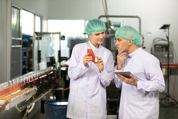 twee fabrieksarbeiders praten over project en kwaliteitscontrole van basilicumzaaddrank in drankenfabriek - Foto, afbeelding