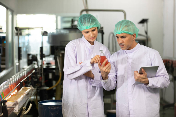 kaksi tehdastyöntekijää puhuu projektista ja tarkistaa basilikan siemenjuoman laatua juomatehtaalla - Valokuva, kuva