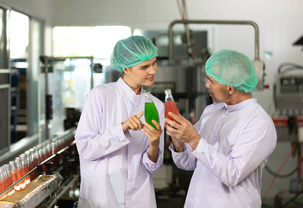 two factory workers talking about project and checking quality of basil seed drink in beverage factory - Photo, Image