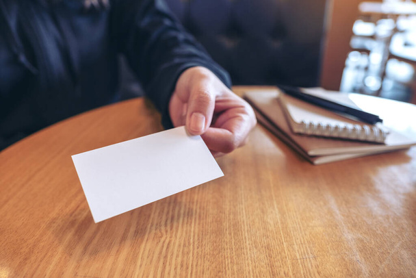 A woman holding and giving a blank empty business card to someone with notebooks on table - Photo, Image