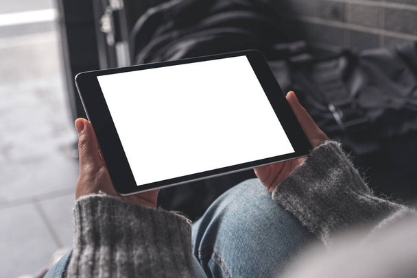 Imagen burlona de las manos de la mujer sosteniendo y usando una tableta negra PC con pantalla de escritorio blanca en blanco mientras está sentada en el suelo con equipaje - Foto, imagen