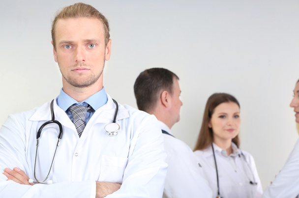 Lääkäri seisoo harmaalla pohjalla olevien työtovereiden edessä
 - Valokuva, kuva