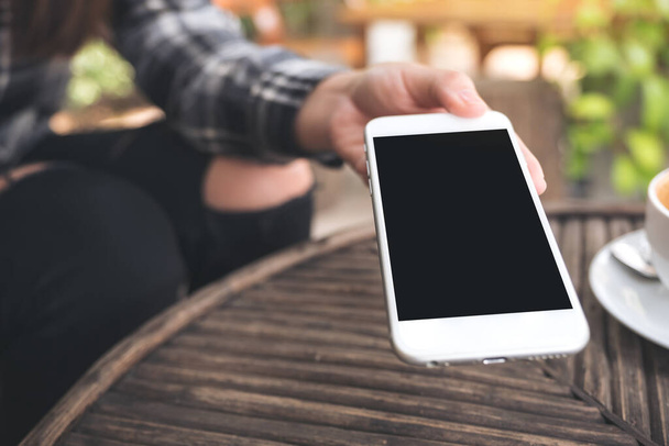 Image de maquette d'une main tenant et donnant un téléphone portable blanc avec écran noir blanc de bureau à quelqu'un dans un café - Photo, image