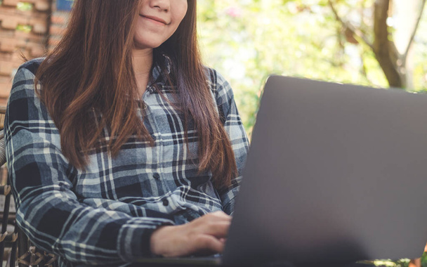 Uma bela mulher asiática usando e digitando no laptop enquanto sentado ao ar livre  - Foto, Imagem