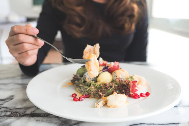 Žena si vychutnává míchaný ovocný salát se smaženými krevetami na stole v restauraci - Fotografie, Obrázek