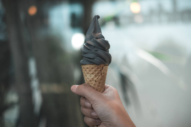 Рука тримає вугільний конус морозива з розмитим фоном
 - Фото, зображення