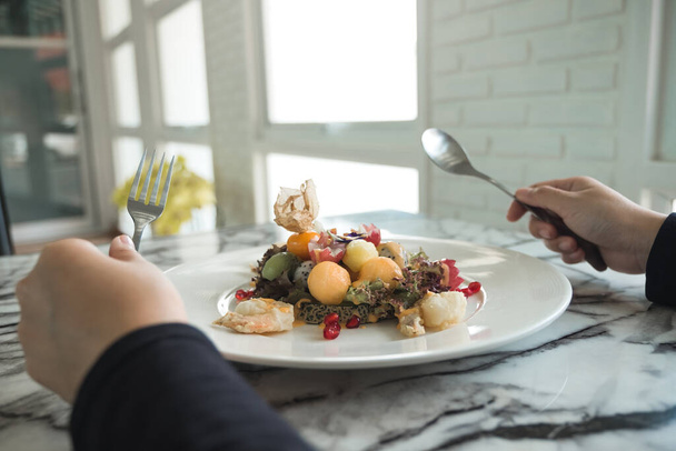 Женщина, держащая ложку и вилку и готовясь есть салат из смешанных фруктов с жареными креветками на столе в ресторане - Фото, изображение