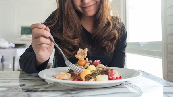 Een mooie aziatische vrouw geniet van het eten van fruit salade op de tafel in restaurant - Foto, afbeelding