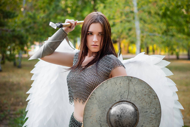 Portrait of a warrior woman in chain mail with steel bracers and wings behind her back. Standing in a fighting position with a spear and a shield in his hands. - Φωτογραφία, εικόνα