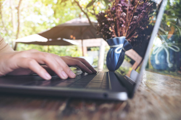 Imagen de cerca de las manos trabajando y escribiendo en el teclado del ordenador portátil en la mesa de madera en la cafetería  - Foto, imagen