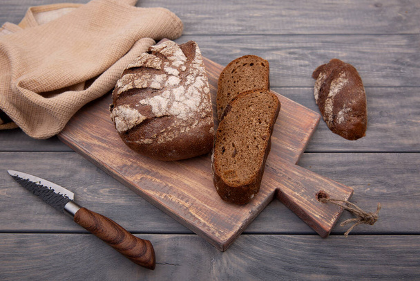Rye bread round loaf cut into pieces on a wooden board with a knife made of rustic wood. Top view. - Foto, imagen