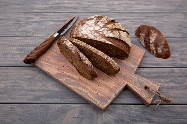 Rye bread round loaf cut into pieces on a wooden board with a knife made of rustic wood. Top view. - 写真・画像