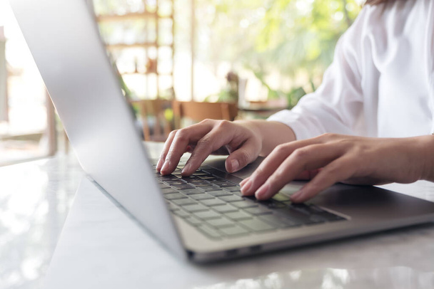 Imagem de close-up das mãos da mulher trabalhando e digitando no teclado do laptop na mesa com fundo natureza borrão - Foto, Imagem