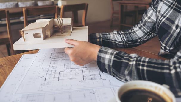 Un arquitecto sosteniendo y trabajando en el modelo de arquitectura con papel de dibujo de tienda en la mesa - Foto, imagen