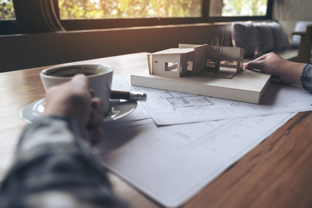 Un arquitecto trabajando en un modelo de arquitectura con papel de dibujo de tienda mientras bebe café - Foto, imagen