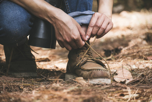Closeup image of a man tying shoelace while trekking in a tropical forest - Photo, Image