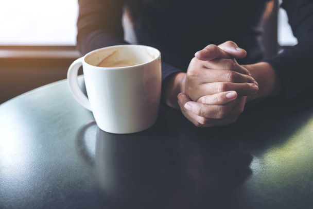 Szoros kép egy nőről, aki fogja a kezét és forró kávét iszik a kávézóban. - Fotó, kép