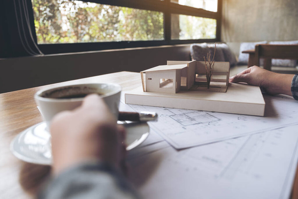 Архитектор, работающий над архитектурной моделью с бумагой для рисования в магазине, пьющий кофе в офисе - Фото, изображение