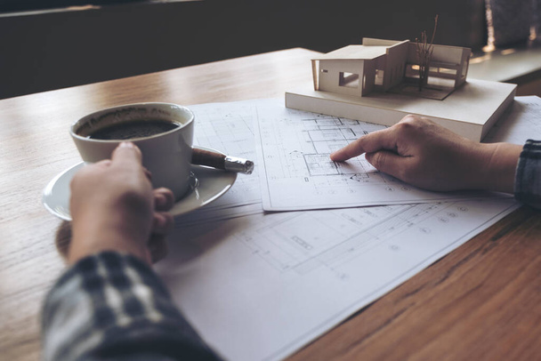 Een architect die werkt aan een architectuurmodel met tekenpapier tijdens het drinken van koffie op kantoor - Foto, afbeelding