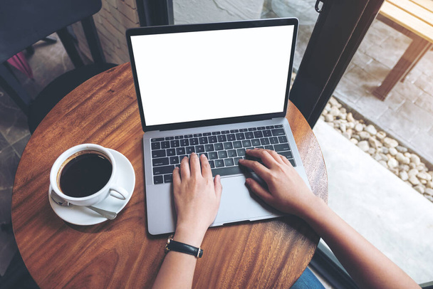 Visualizzazione dall'alto immagine mockup di una donna che utilizza e digita su laptop con schermo desktop bianco vuoto su tavolo in legno nel caffè - Foto, immagini