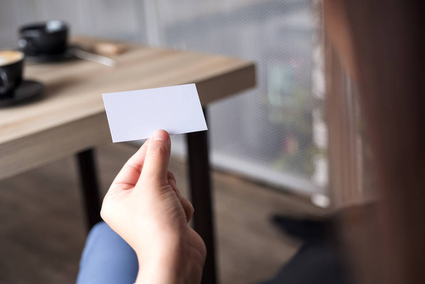 Empresaria sosteniendo una tarjeta de visita vacía mientras está sentada en la oficina - Foto, Imagen