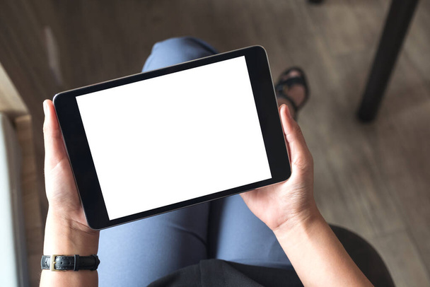 Vue du dessus image maquette d'une femme assise jambes croisées et tenant tablette noire pc avec écran blanc vierge de bureau dans le bureau - Photo, image