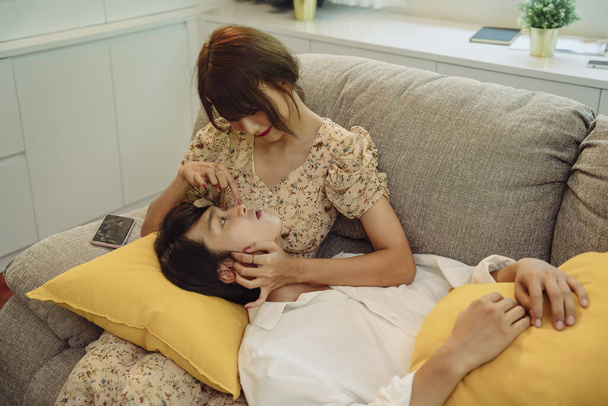 Ρομαντικό σκηνικό. Ασιατικό ταϊλανδέζικο ζευγάρι στο σαλόνι. Άντρας ξαπλωμένος στην αγκαλιά της γυναίκας στον καναπέ. - Φωτογραφία, εικόνα