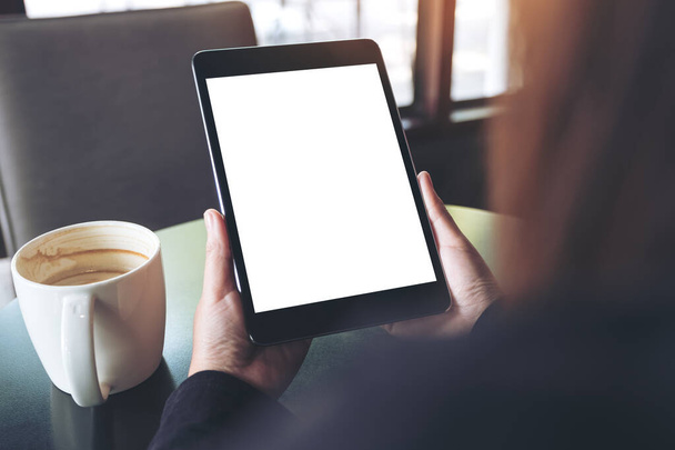 Макетне зображення рук, що тримають чорний планшетний ПК з порожнім білим екраном і чашкою кави на столі в кафе
  - Фото, зображення