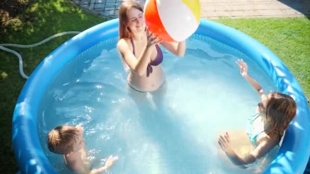 Vista dall'alto di bambini allegri felici con madre che gioca a pallavolo in piscina gonfiabile a giardino di cortile di casa. Concetto di vacanze estive felici e allegre e vacanze - Filmati, video