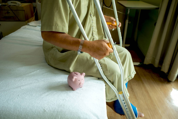 Поросячья копилка с мужской ногой использует костыли, чтобы ходить после операции восстановления сломанных костей. - Фото, изображение