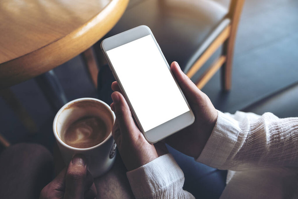 Imagem Mockup das mãos de duas pessoas segurando telefone celular branco com tela de desktop em branco e uma xícara de café  - Foto, Imagem