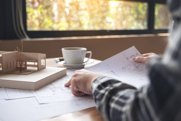 Een architect die werkt aan een architectuurmodel met tekenpapier en koffiebeker op tafel - Foto, afbeelding