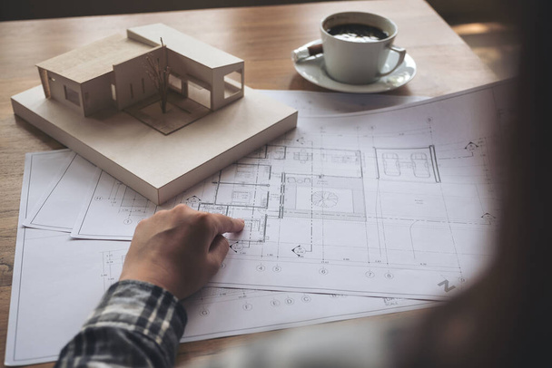 テーブルの上に紙とコーヒーカップを描く店の建築模型に取り組む建築家 - 写真・画像