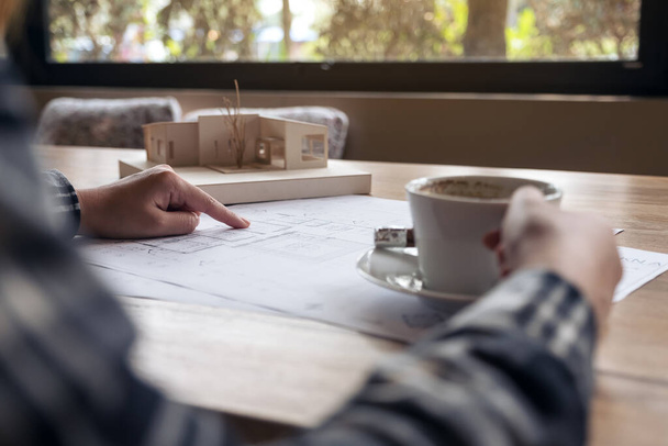 Un architecte travaillant sur un modèle d'architecture avec du papier dessin de magasin tout en buvant du café au bureau - Photo, image
