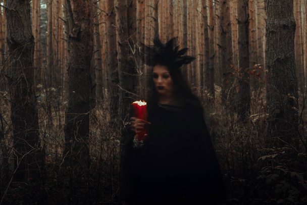 Ведьма в черном костюме колдует при свечах в лесу. - Фото, изображение