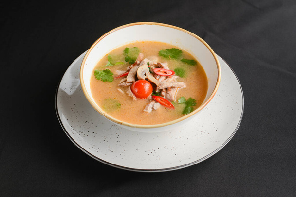 Mushroom soup of chicken broth, mushrooms, cherry tomato served in a white bowl over black background. Dinner concept, healthy hot soup. - Photo, image
