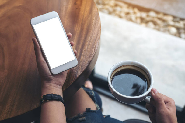 喫茶店でコーヒーを飲みながら白い携帯電話を持っている女性の手のモックアップイメージ - 写真・画像