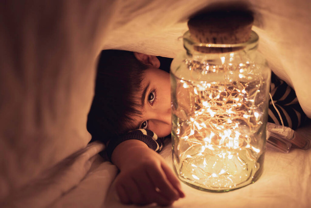 Ребенок играет под простыней с кастрюлей теплых огней Концептуальный образ жизни, детская игра дома - Фото, изображение