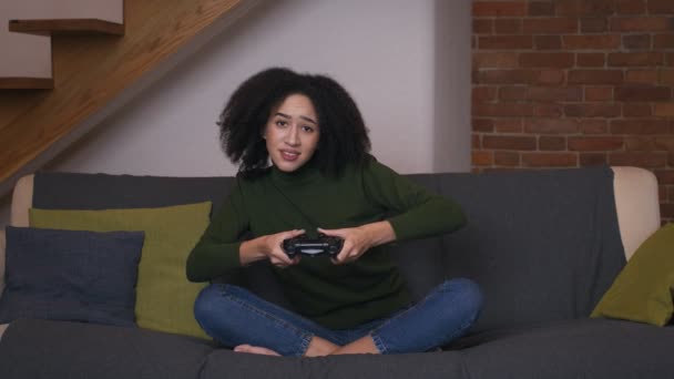 Emocionado jugador afroamericano mujer jugando videojuegos en casa y disfrutando de ganar, sentado en el sofá con joystick - Imágenes, Vídeo