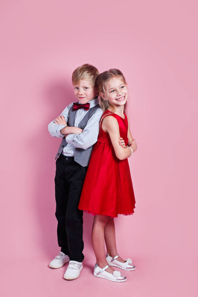 День Святого Валентина. Милый улыбающийся мальчик и девочка стоят на розовом фоне . - Фото, изображение