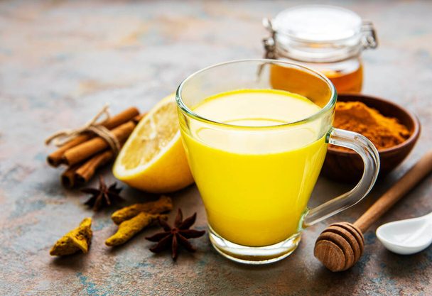 Yellow turmeric latte drink. Golden milk with cinnamon, turmeric, ginger  and honey over concrete background. - Valokuva, kuva