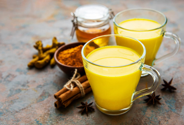 Yellow turmeric latte drink. Golden milk with cinnamon, turmeric, ginger  and honey over concrete background. - Foto, Bild