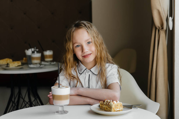 A cute little girl is sitting in a cafe and looking at a cake and cocoa close-up. Diet and proper nutrition - Foto, Imagem