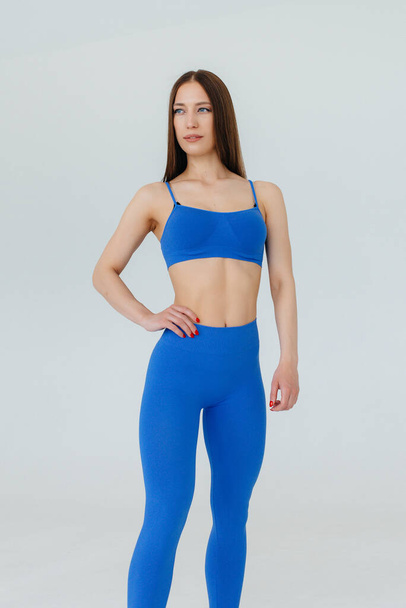Sexy young girl posing in a blue tracksuit on a white background. Fitness, healthy lifestyle - Valokuva, kuva