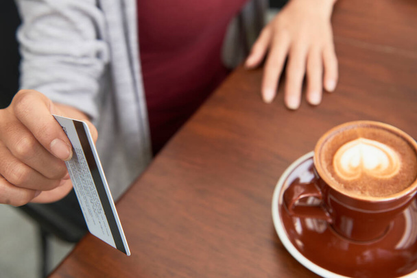 Женщина-клиент готова украсть свою кредитную карту при оплате чашки капучино в кофешопе - Фото, изображение
