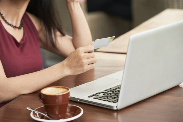Imagen recortada de la joven sentada en la cafetería con taza de café y computadora portátil y haciendo compras en línea - Foto, Imagen