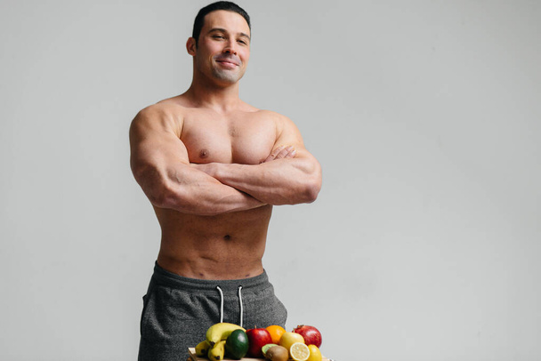 Sexy vegan guy with a naked torso posing in the Studio next to fruit. Diet. Healthy diet - Foto, imagen