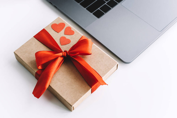 Gift box with red ribbon and hearts on the table near laptop. Valentine's day surprise concept - Fotoğraf, Görsel