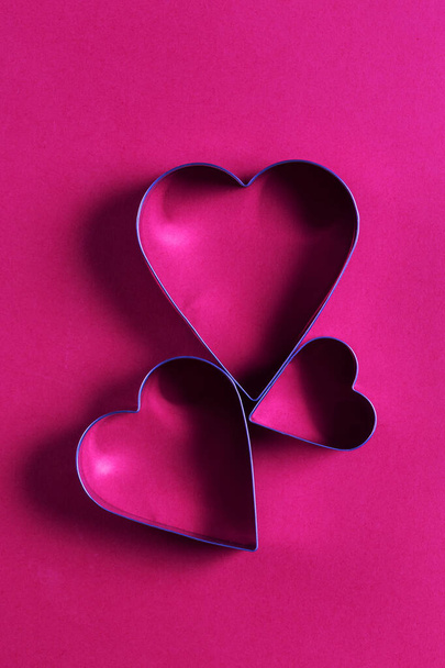 Saint Valentine day minimalistic greeting card, heart-shaped cookie cutters on pink magenta background with beautiful shadows, flat lay - 写真・画像